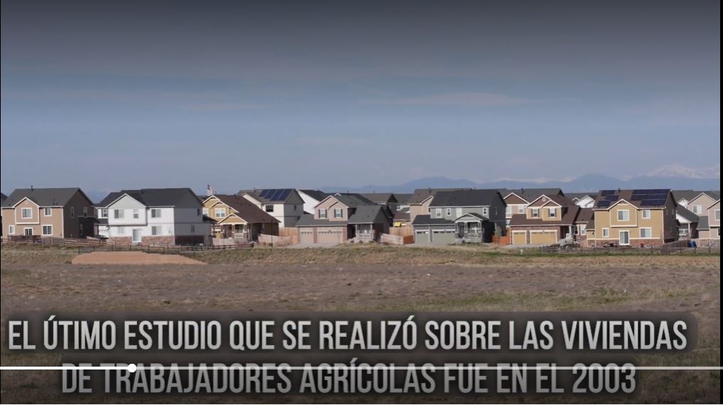 Suburban development with houses in view and mountains in the background, with Spanish text overlay about an agricultural workers' housing study from 2003