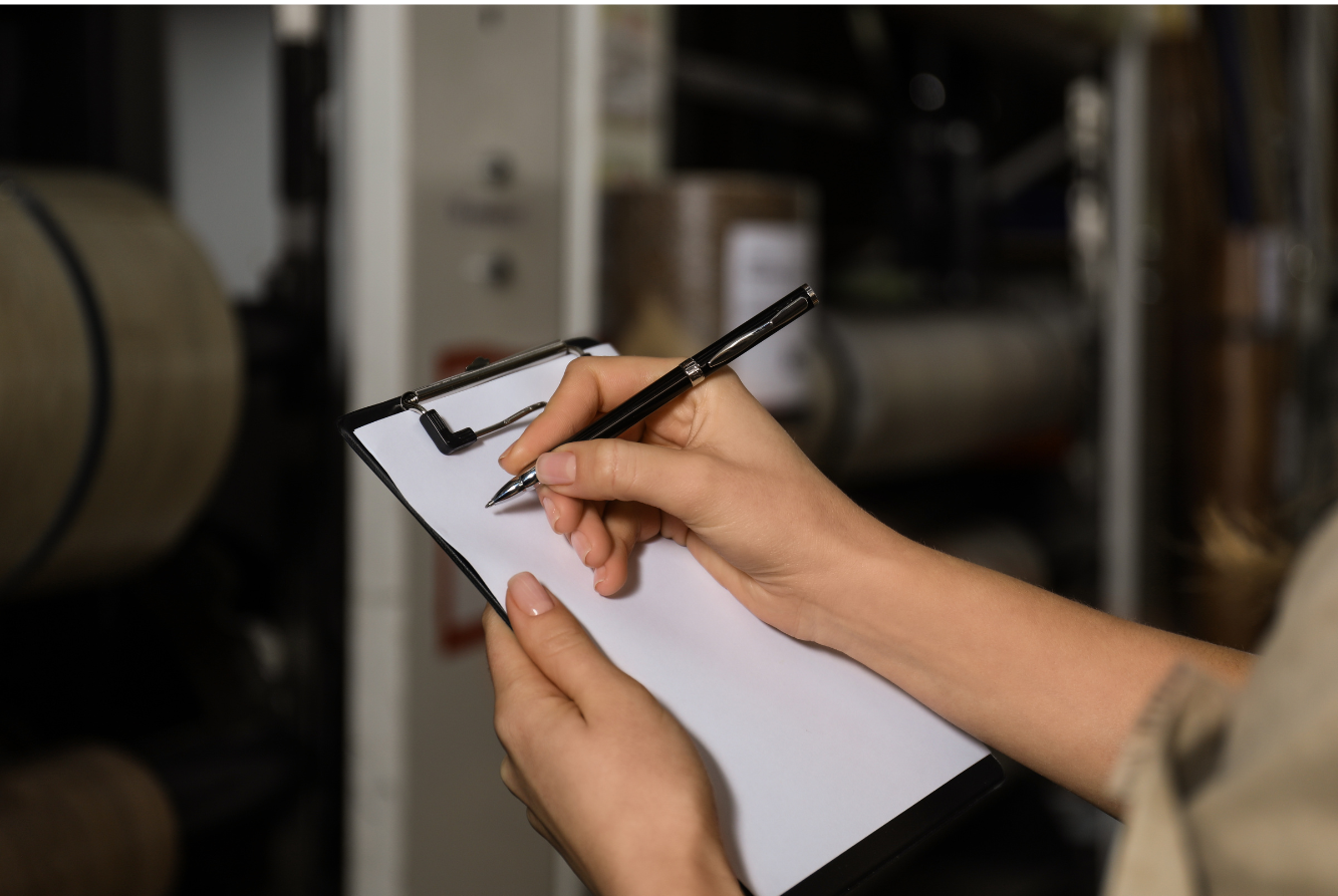 A person writing on a piece of white paper on a clipboard with a pen.