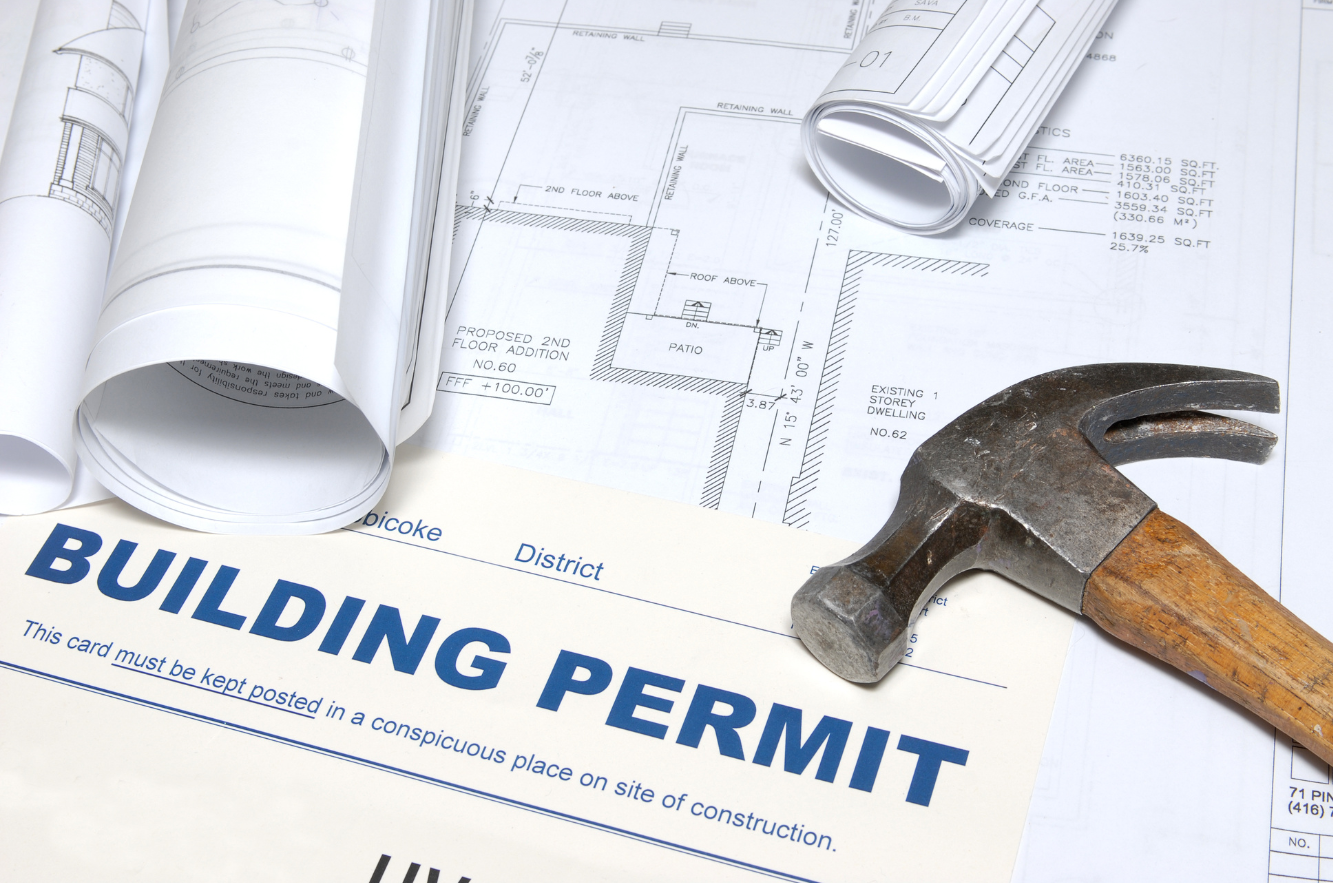 A building permit placed on top of architectural plans and blueprints with a hammer nearby.