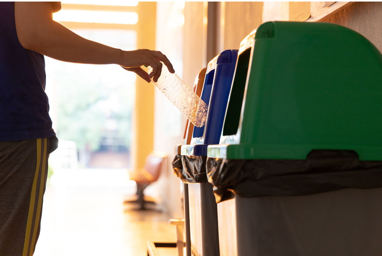 A person recycling a plastic bottle into the blue bin, this display 3 colorful bins like yellow, blue, and green.