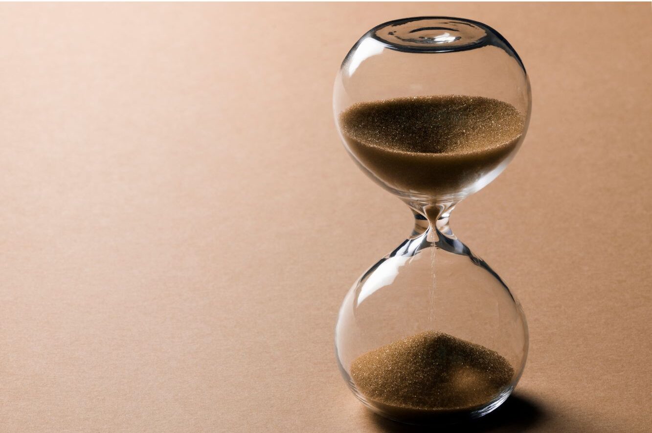 A transparent hourglass with sand flowing from the upper half to the lower half on a beige background.