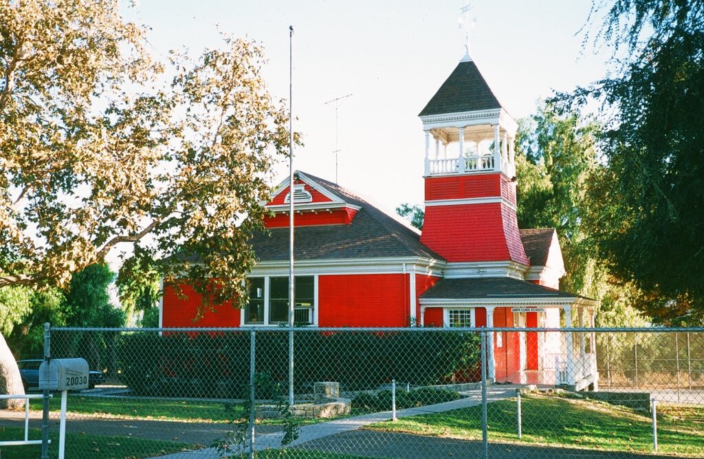 Santa Clara Schoolhouse, a red building with a prominent tower, set behind a fence, 1985.