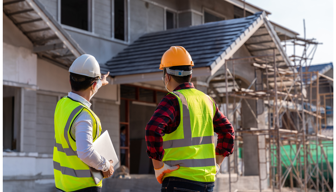 Two construction workers with safety vests and hard hats inspecting a building under construction.