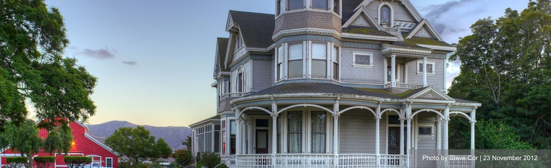 Victorian-style house with an ornate turret and wrap-around porch, set against a backdrop of a clear sky.