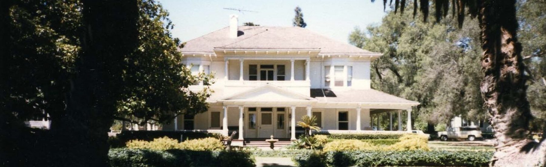 Front view of the Lloyd-Butler House, a historic two-story residence with wraparound porch and lush landscaping, 1986.